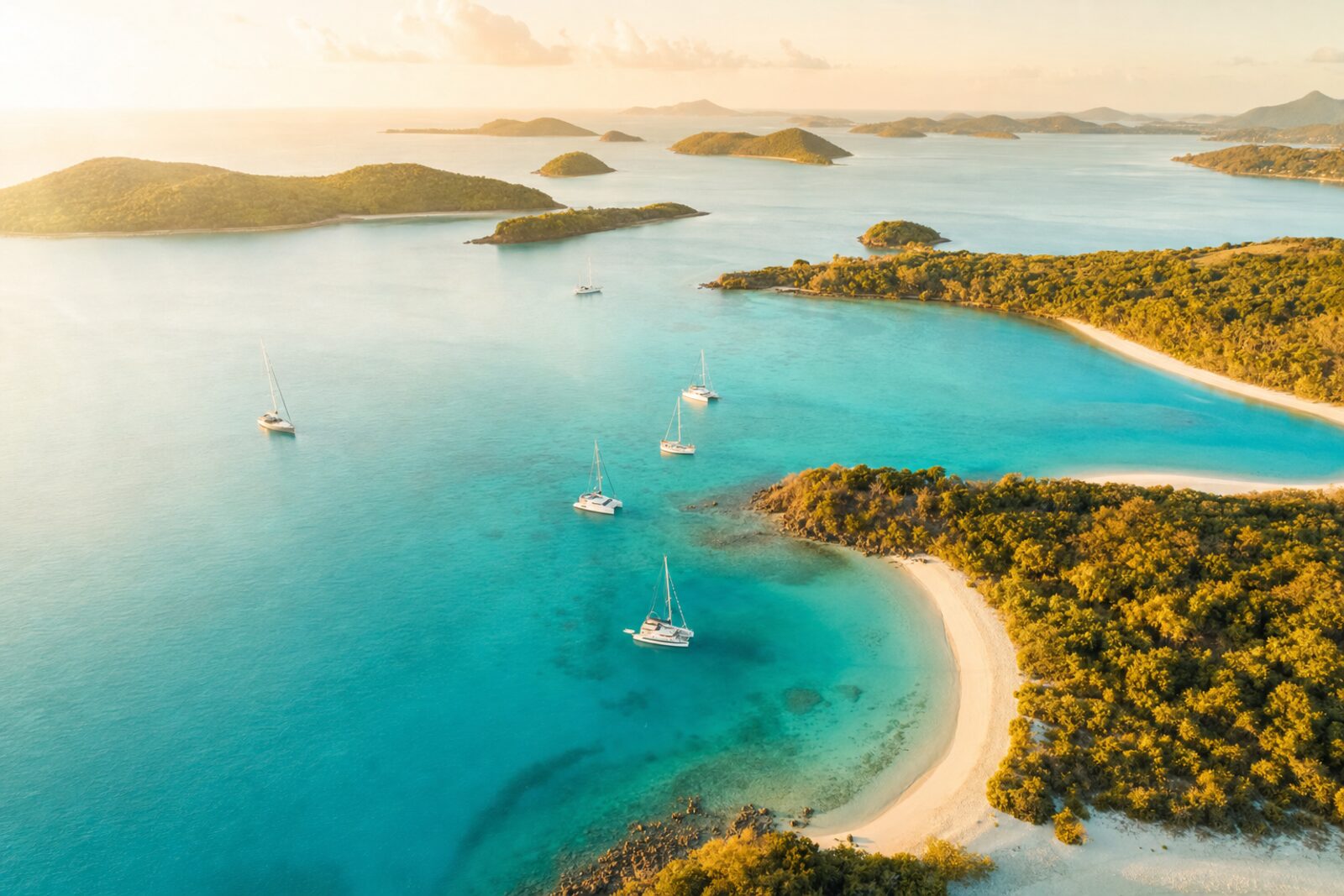 Aerial view of a turquoise bay dotted with tropical islands and sailboats at golden hour